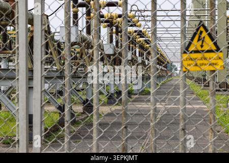 Netherlands: Industrial view of a high voltage electrical power grid substation with a yellow danger warning sign on the fence. Stock Photo