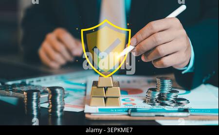 Businessman using stylus pen pointing at virtual shield checkmark icon on gold bars. Financial security, wealth protection, asset management and inves Stock Photo