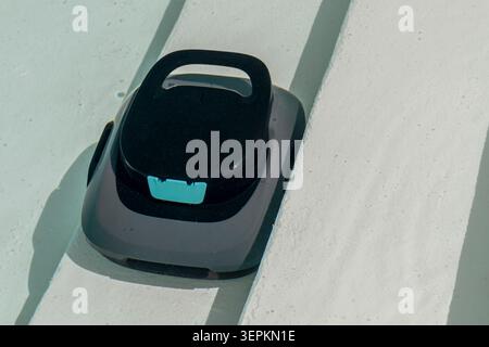A cordless pool cleaner is cleaning the steps of an inground pool Stock Photo