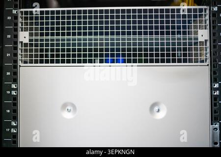 This image displays a section of a server or computer rack, featuring a metal grid panel and a smooth white panel with two visible screws, used in dat Stock Photo