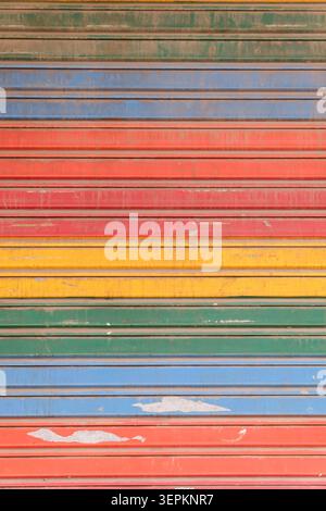 Multicoloured painted corrugated metal rolling shutter door with weathered peeling paint in bands of red, orange, yellow, green and blue, Old Delhi. Stock Photo