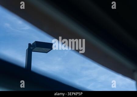 This image features a modern street lamp standing against a bright blue sky with light clouds, highlighting urban infrastructure and cityscape element Stock Photo