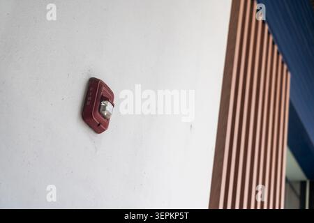 A modern fire alarm is mounted on a plain white wall with part of a wooden slatted partition and ceiling visible. It is essential for building safety Stock Photo