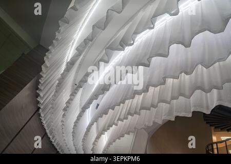 The image displays a striking modern interior ceiling with flowing, wave-like architectural panels illuminated by soft natural light, creating an inno Stock Photo