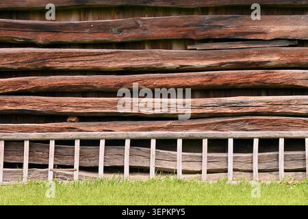 Background of rustic wooden wall with weathered uneven horizontal logs, ladder and green grass Stock Photo