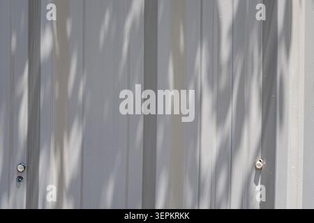 This image displays a metal wall surface with shadows cast by vertical structural elements, creating an abstract pattern of light and shade in a moder Stock Photo