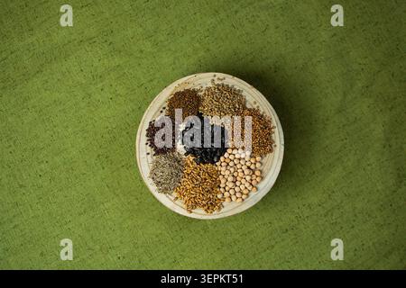 Overhead view shows clear separation of multiple seed types on plate. Seed variety flat lay on plate with green textile. Rustic ceramic holds nine sep Stock Photo