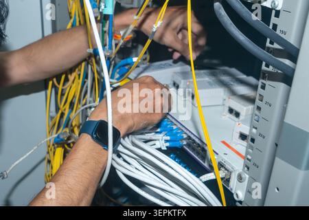 Two technicians are working on a complex network server setup with tangled cables and electronic components in a data center environment, focusing on Stock Photo