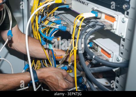 A technician working on a server rack with multiple network cables and hardware components, performing maintenance or setup in a data center or networ Stock Photo