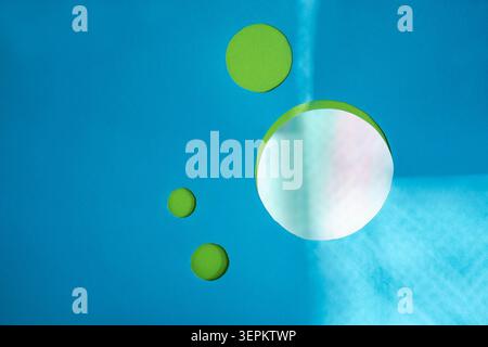 Paper cutout elements create tactile, handcrafted quality within minimalist geometric composition. Paper cut green circles with mirror disc on turquoi Stock Photo