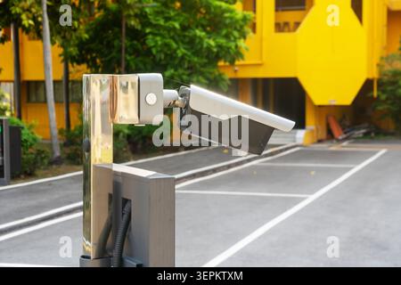 The image shows a modern outdoor security camera mounted on a metal stand, installed in a parking lot for surveillance, monitoring, and safety purpose Stock Photo