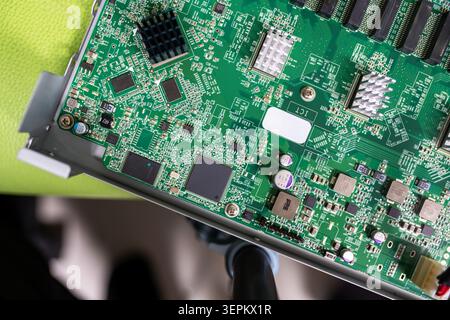 Close-up of a green printed circuit board featuring various electronic components, chips, resistors, capacitors, and connectors ready for device assem Stock Photo