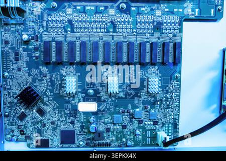 Detailed image of a blue printed circuit board featuring various electronic components, connectors, microchips, capacitors, resistors, and wiring. Stock Photo