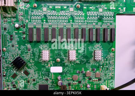 Close-up photograph of a green printed circuit board featuring numerous microchips, electronic components, and soldered connections, illustrating mode Stock Photo