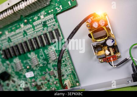 Detailed image showing a close-up view of an electronic circuit board with embedded components, wiring, and a LED indicator on a gray background. Stock Photo