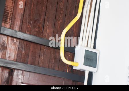Close-up of an electrical meter box with yellow and white pipes mounted on a wooden wall, illustrating utility infrastructure and electrical system co Stock Photo
