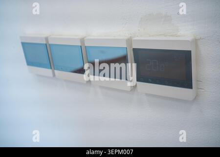 The image features a sleek, modern wall-mounted digital thermostat with multiple screens displaying temperature settings in a contemporary interior sp Stock Photo