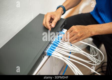 A technician managing network cables on a patch panel, performing connection tasks in a professional office environment for efficient data and interne Stock Photo