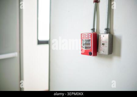 The image features a fire alarm system mounted on a smooth, white interior wall, including a red alarm box and a metal electrical junction box, symbol Stock Photo