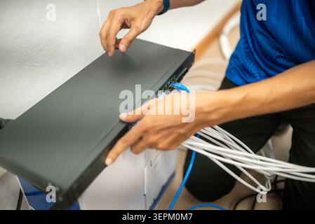 A technician is connecting and managing network cables on a black network device, working on server infrastructure in an indoor setting with a focus o Stock Photo