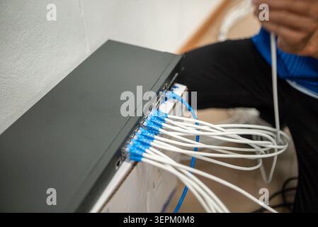 A network technician installing and managing ethernet cables connected to network equipment, demonstrating technical work in establishing computer con Stock Photo