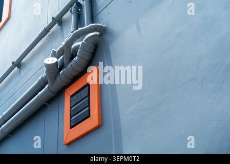 This image shows industrial ventilation pipes and an orange vent cover mounted on a light blue factory wall, illustrating infrastructure and building Stock Photo
