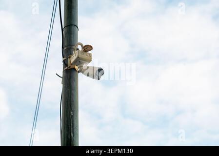 A security surveillance camera mounted on a utility pole captures the outdoor environment against a partly cloudy sky, showcasing modern security tech Stock Photo