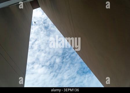 This photo captures a low-angle view of two tall modern buildings with concrete walls framing the open sky. The scene highlights urban architecture, c Stock Photo