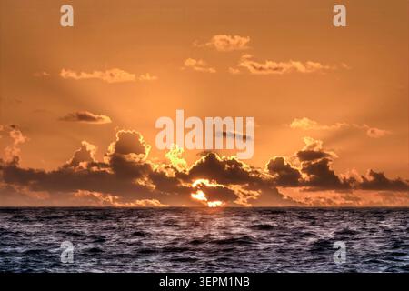Sun rising through clouds over Atlantic Ocean Stock Photo