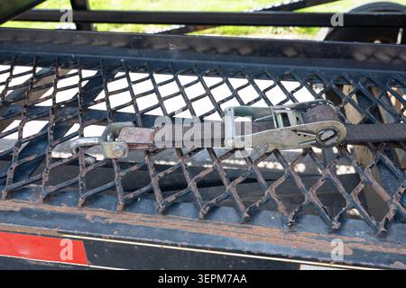 Close-up photo of a metal trailer with a rusty diamond-patterned grid surface, featuring a ratchet tie-down strap laid across it Stock Photo