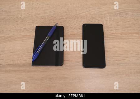 Black notebook, blue pen and mobile phone on wooden desk Stock Photo