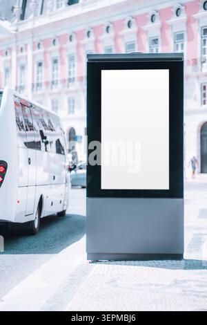 Blank vertical advertising lightbox mockup on a sunny city sidewalk beside a white bus, with pastel historic facade and street traffic in the backgrou Stock Photo