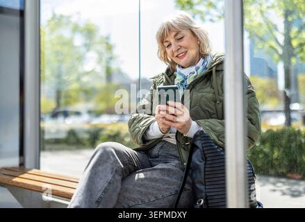 Woman using her smartphone while waiting for a bus in the city Stock Photo