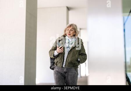 Mature woman walking in city with mobile phone Stock Photo