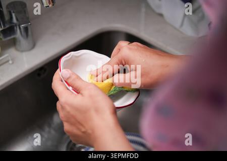 Cleaning a bowl at the kitchen sink in the evening Stock Photo