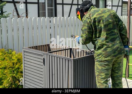 Man wearing protective welding mask, gloves, workwear using welding machine outdoors in residential yard. Repairing box, concept of safe welding, DIY Stock Photo