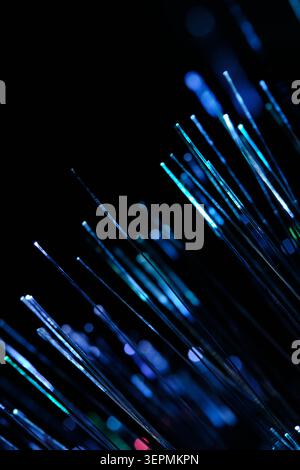Vertical composition bright blue fiber optics shining and creating beautiful bokeh on black canvas Stock Photo
