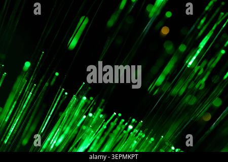 Deep green glowing fiber optic wires creating dynamic pattern against dark setting with abstract bokeh Stock Photo
