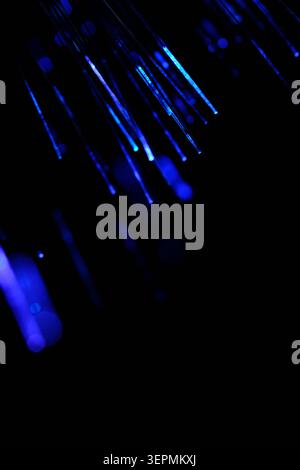 Abstract vertical lines glowing dark blue fiber optic cables shining against black backdrop Stock Photo