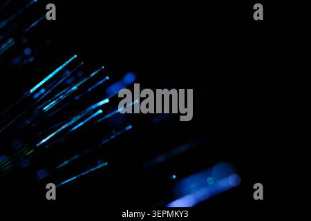 Diagonal blue and cyan glowing fiber optic strands extending out into deep dark space behind Stock Photo