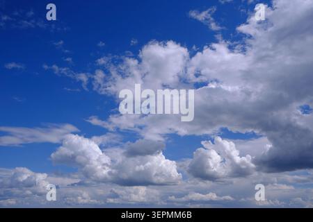 Scattered white clouds floating in wide blue sky on bright, sunny afternoon in summer Stock Photo