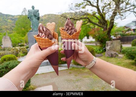 Two hands hold up soft serve milk ice cream waffle cones with chocolate. Iwakuni Japan Stock Photo