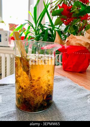 A glass container holds a decoction made from chamomile, yarrow, and corn silk. The setup includes a table, plants, and red decorations making the spa Stock Photo