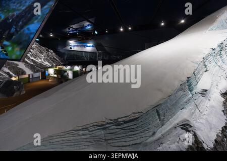 A large-scale glacier model, featuring visible flow structures and crevasses, takes centre stage in a dimly lit exhibition space at the Hohe Tauern National Park Centre (Nationalparkwelten Hohe Tauern) in Mittersill. In the background, screens show supplementary film clips about the glacial world. Gerlos Straße, Klausen, Schattberg, Mittersill, Bezirk Zell am See, Salzburg, 5730, Austria Stock Photo