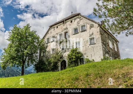 A multi-storey farmhouse with crumbling plaster and a wooden balcony stands on Einödbergweg. A cross on the roof ridge and rubble-stone walls are indicative of the region’s traditional building style. Lämmerbichl, Mittersill, Bezirk Zell am See, Salzburg, 5730, Austria Stock Photo