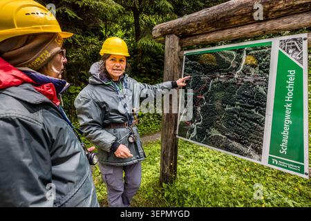At the information board at the Hochfeld exhibition mine in the Untersulzbachtal valley, a guide is explaining the route through the historic copper mine to the visitor, using the overview map. Both are already wearing hard hats for the tour of the tunnels. Rosental, Neukirchen am Großvenediger, Bezirk Zell am See, Salzburg, 5741, Austria Stock Photo