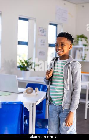African American school-age boy standing right of table in classroom using laptop, copy space Stock Photo