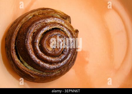 Close-Up Fresh Georgian Cinnamon Roll Pastry On Orange Plate, Bakery Sweet Spiral Breakfast Treat. Stock Photo