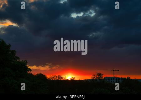 Dramatic Sunset Over Trees and Urban Construction Crane With Dark Storm Clouds on the Horizon Stock Photo