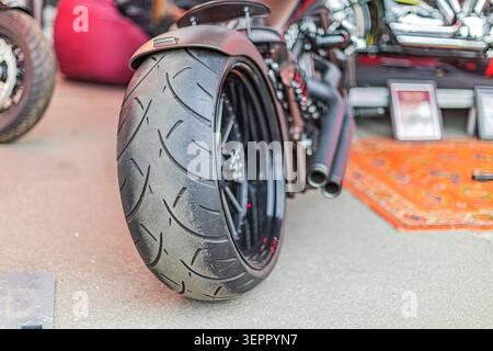 Modern high-performance motorcycle rear view showcasing deep-dish wheel design, textured black tire, red hub accent, polished chrome exhaust pipes, an Stock Photo